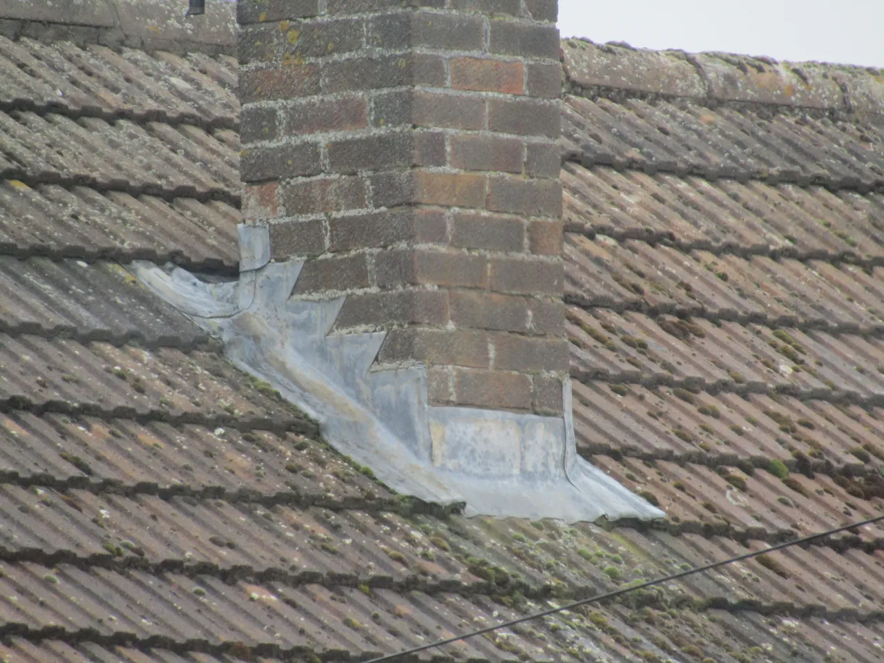 Stepped lead flashing at a brick chimney on a weathered tiled roof