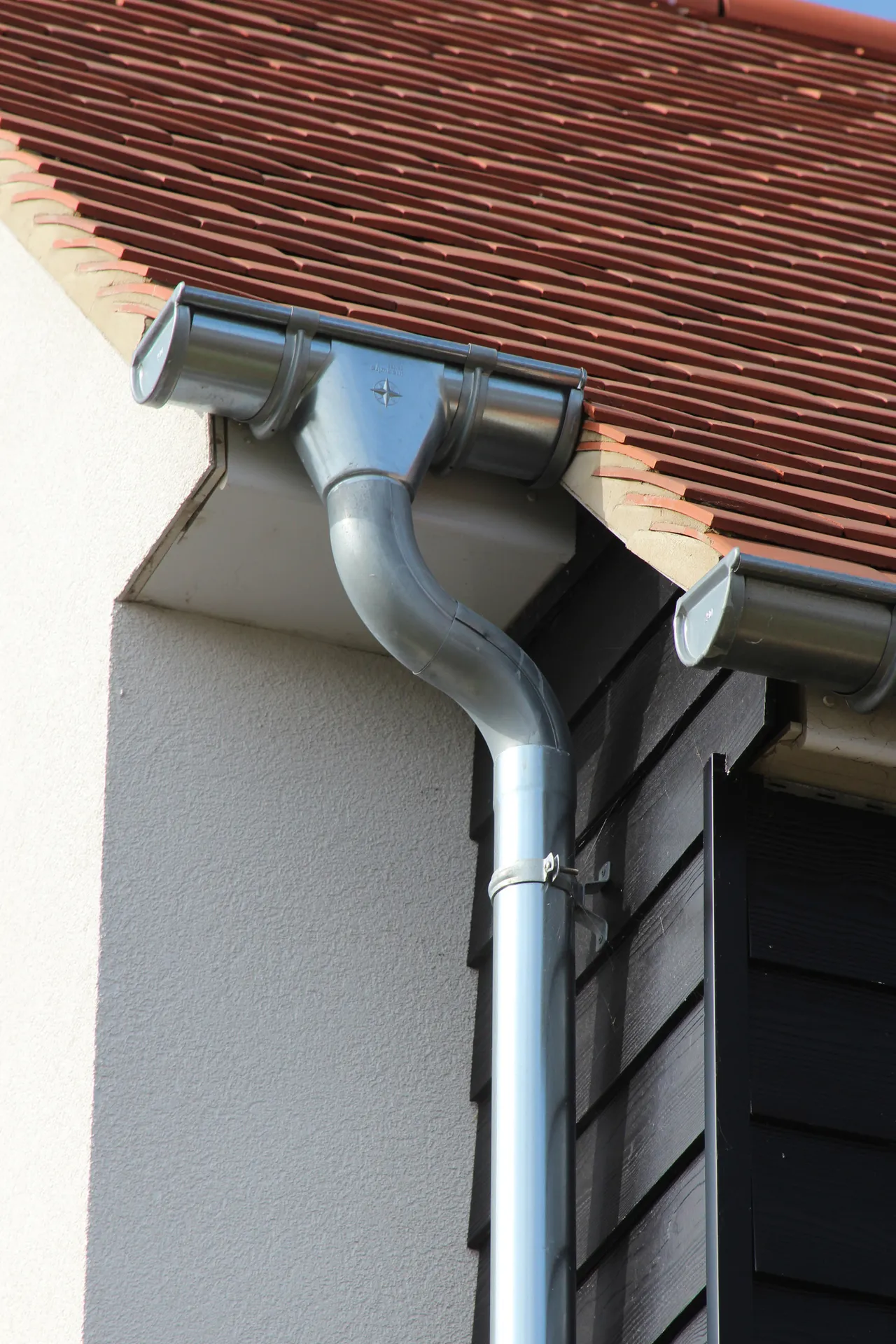 Metal gutter, outlet and downpipe at the eaves of a rendered home