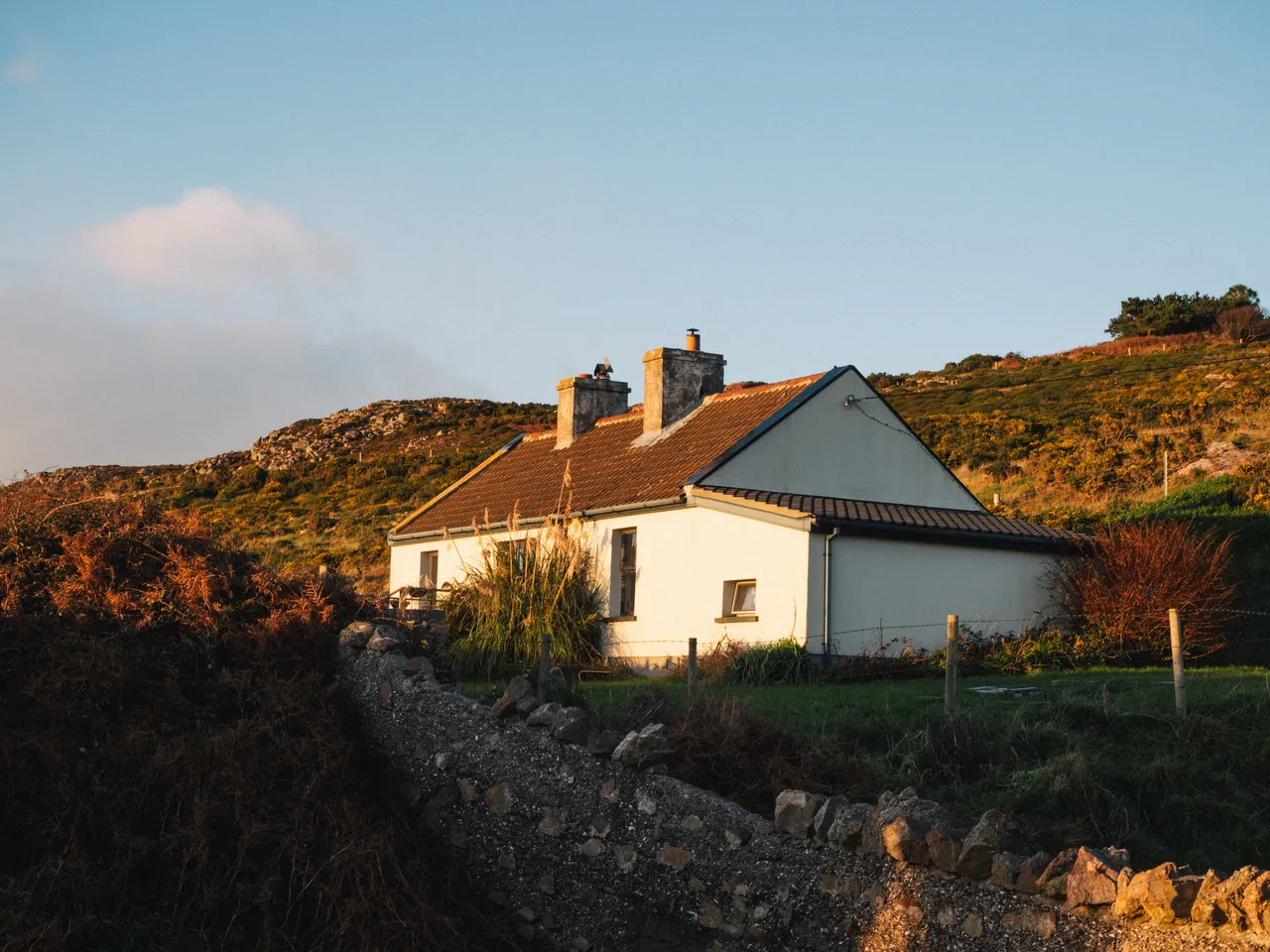 White coastal cottage in Howth with a tiled roof and two chimneys in evening light